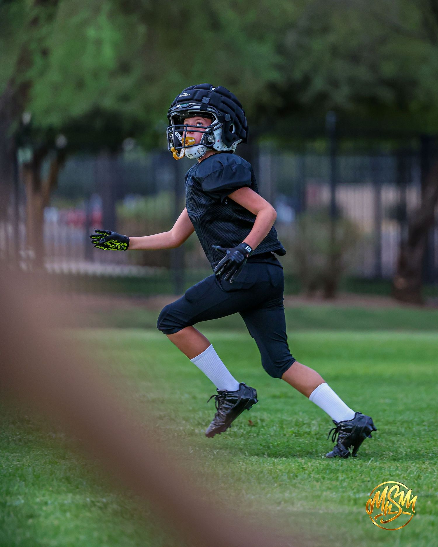 Young football player in black uniform sprints during an outdoor practice session on a grass field.