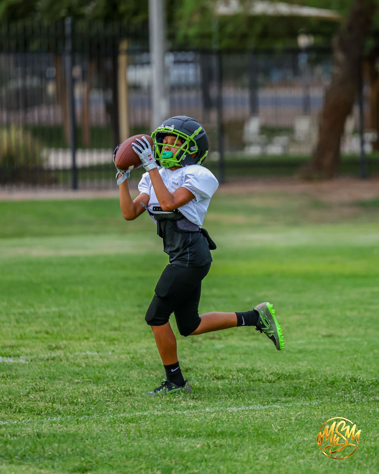 Young football player catches a pass during a youth league practice on a green grass field.