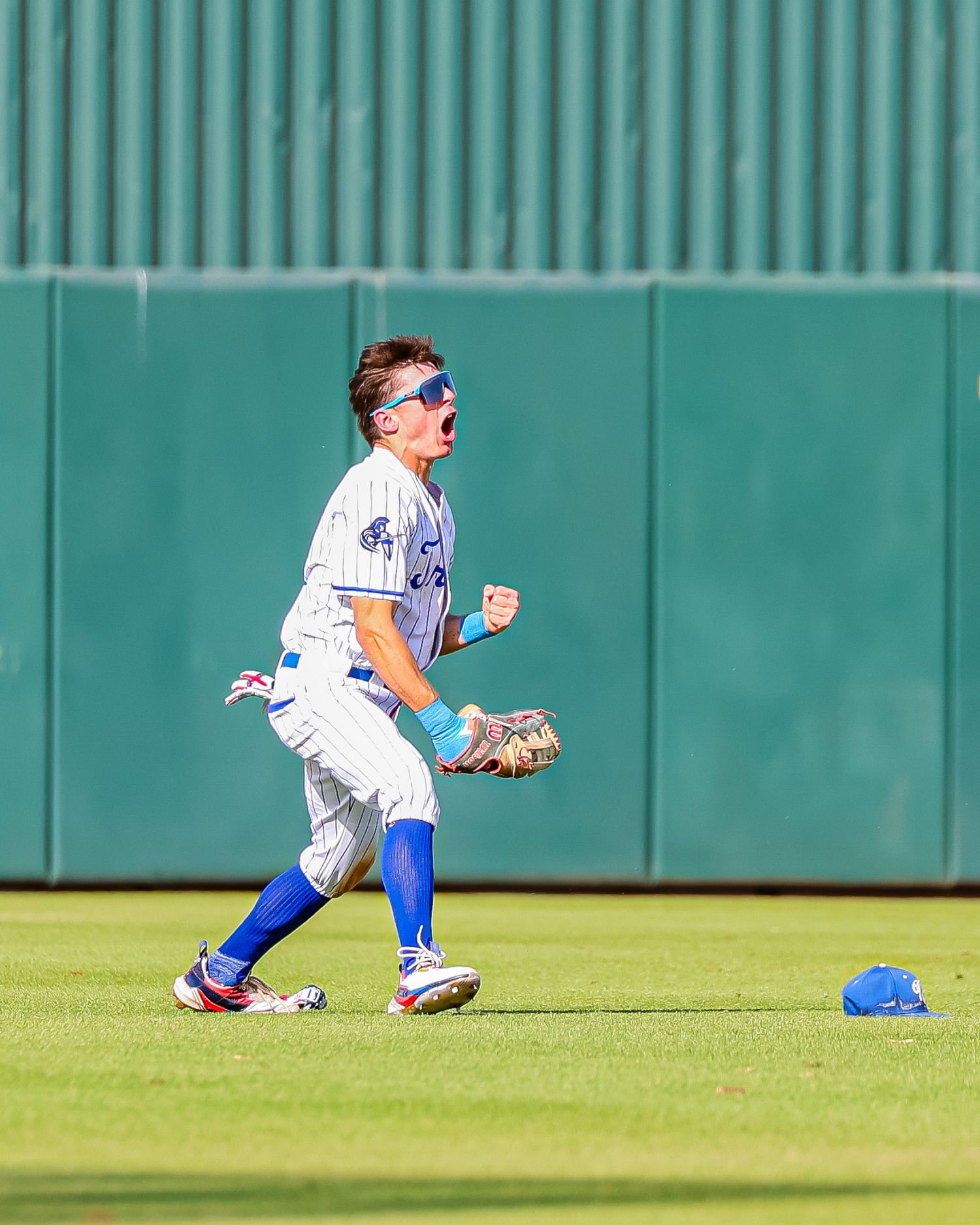Baseball outfielder in blue uniform celebrates a catch while his helmet lies on the grass.