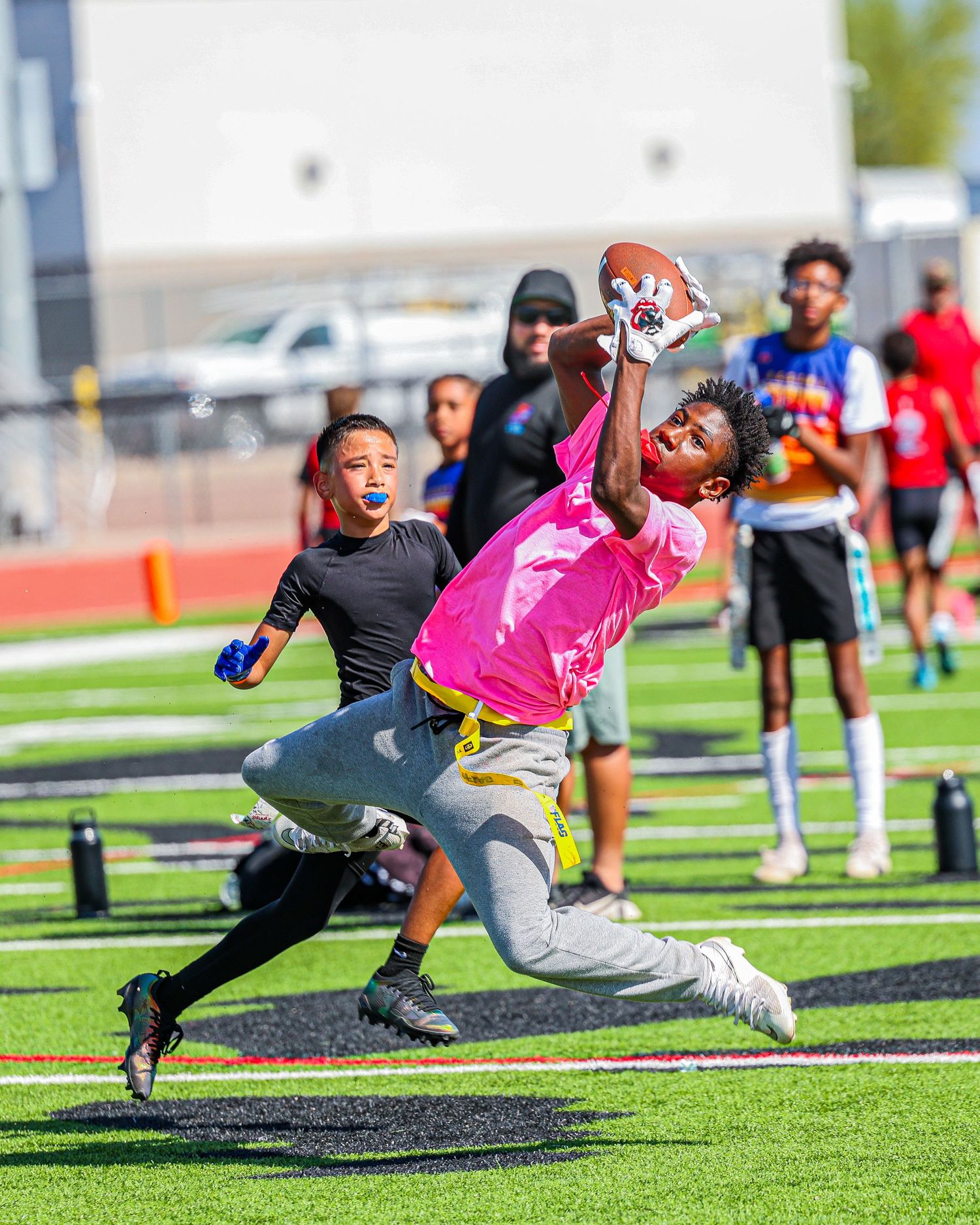 An athlete in pink jersey leaps to make an impressive one-handed catch during a flag football game.