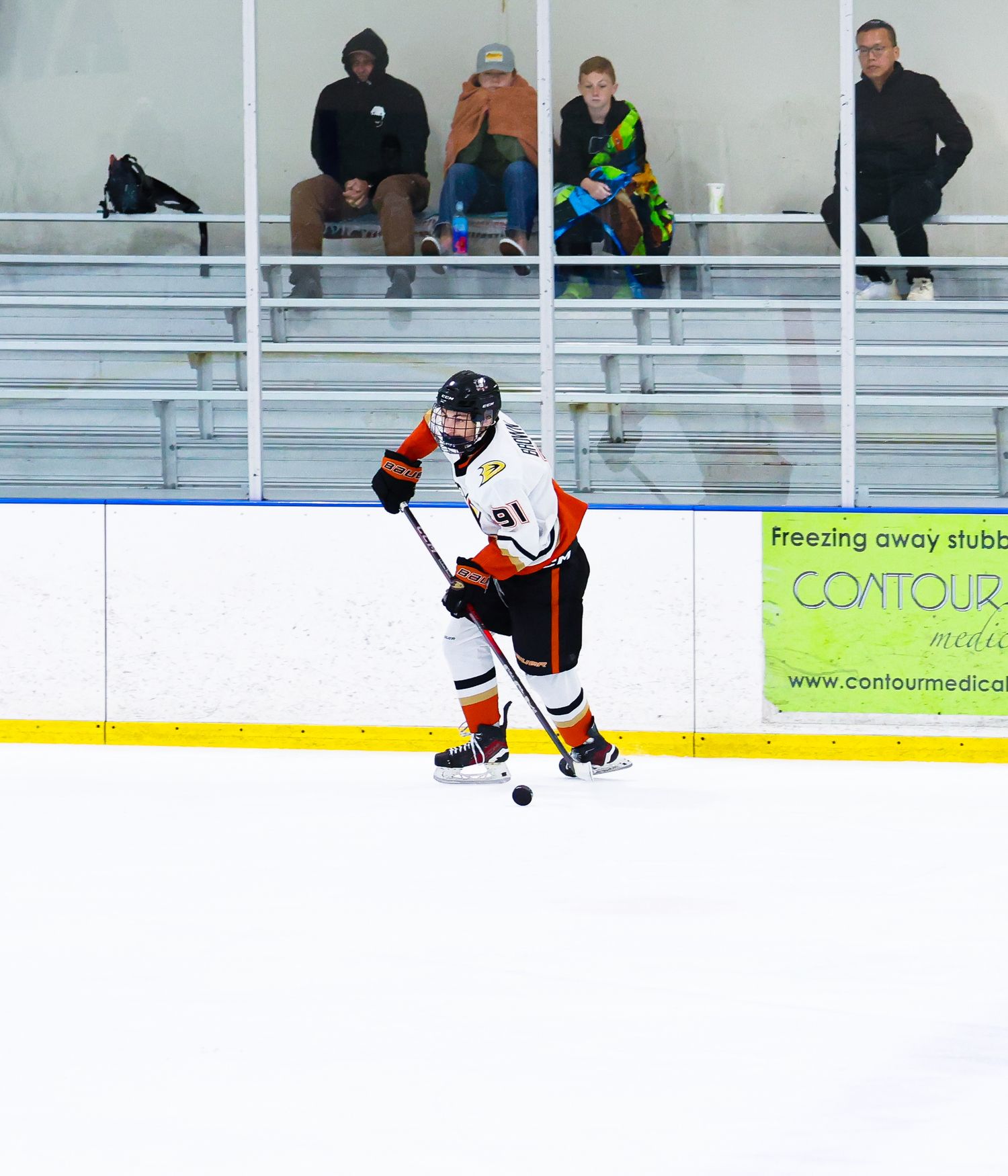 Ice hockey player in orange and white uniform skating with the puck during an indoor rink game.