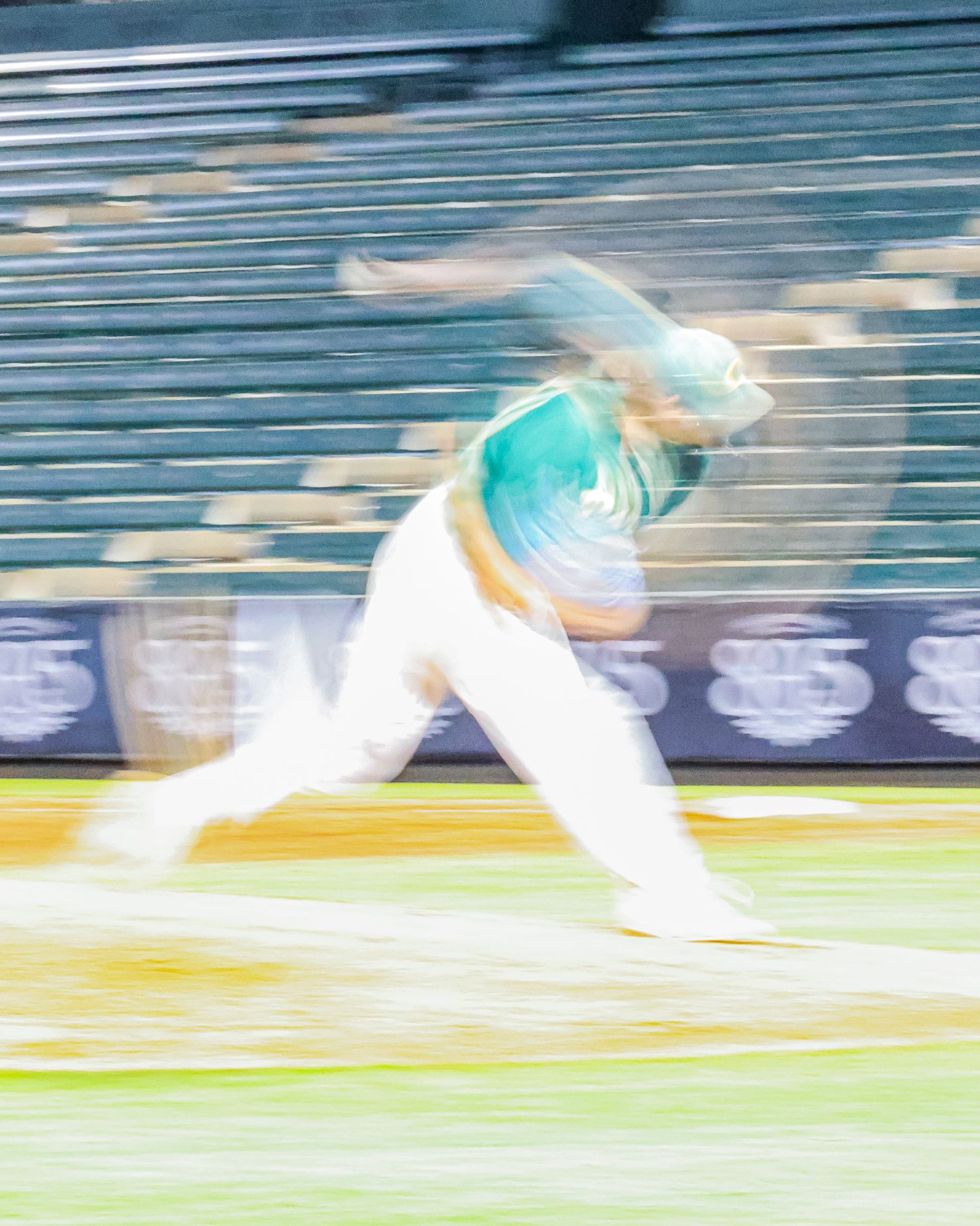 Motion blur action shot of baseball player in teal uniform pitching during game.