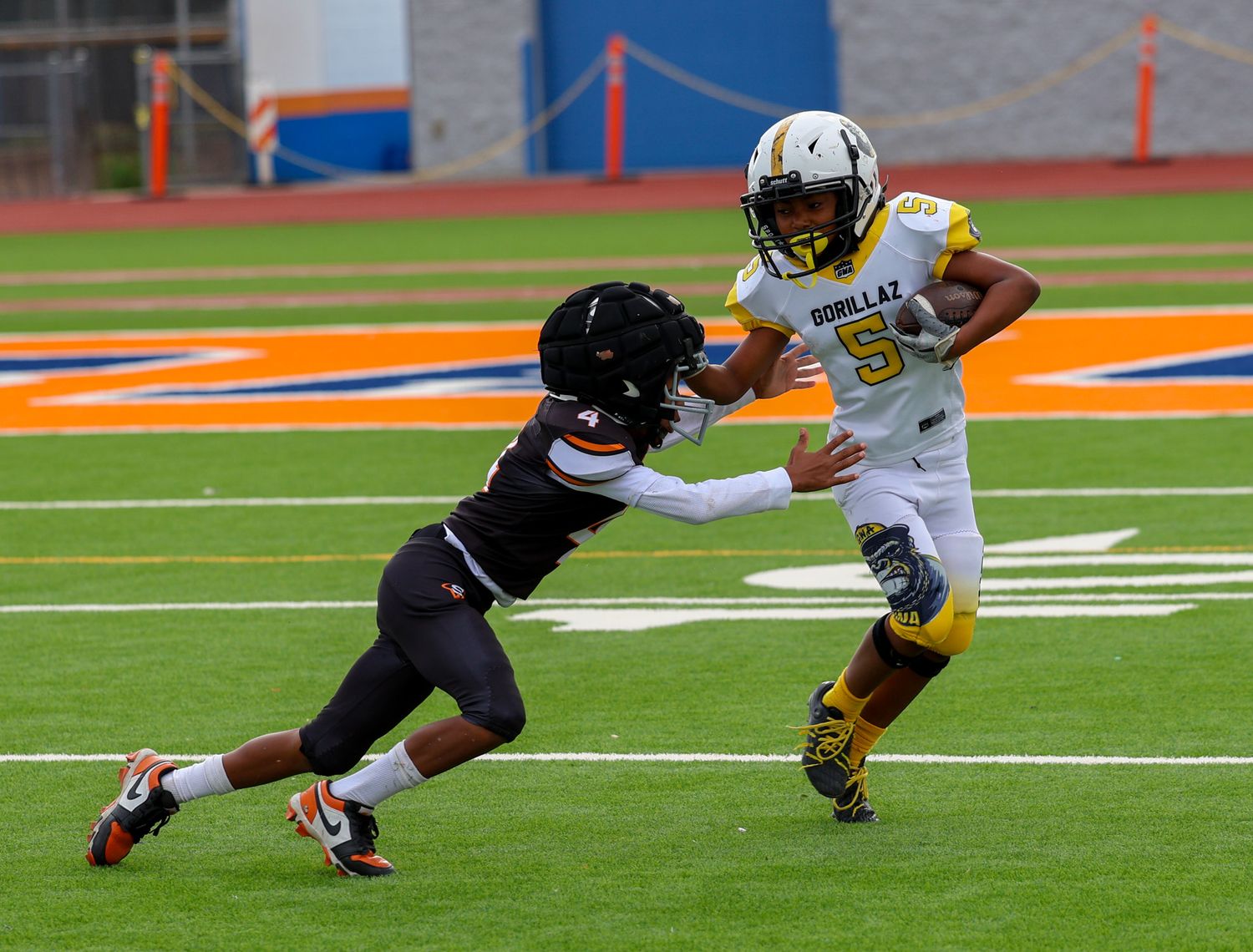 Youth football player in gold #5 jersey breaks away from defender during game.