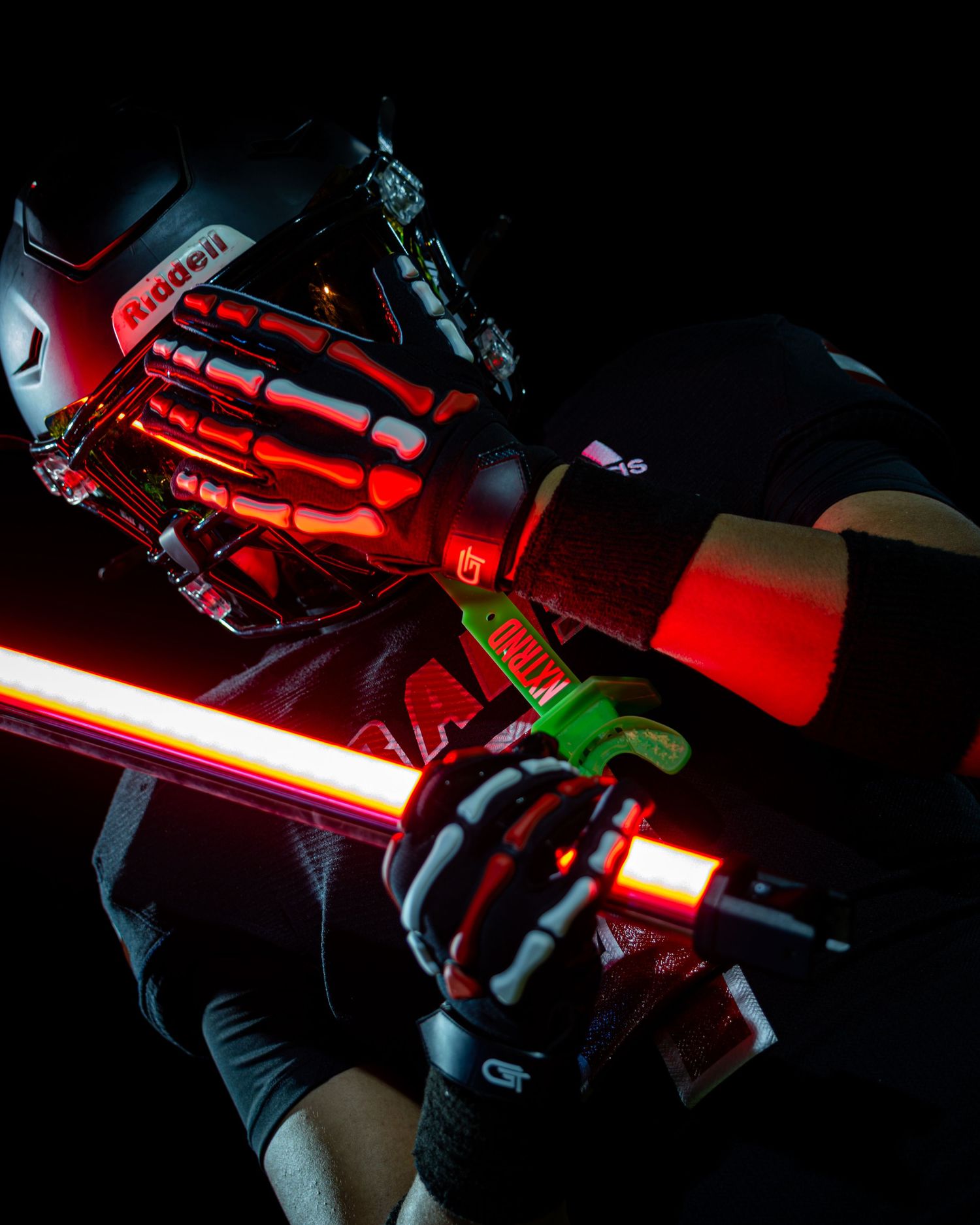 Football player in dark helmet holds glowing red light saber in dramatic night action photo.