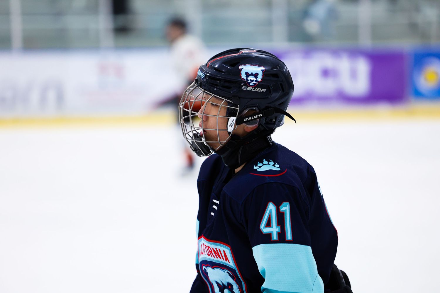 Young ice hockey player wearing number 41 in dark teal uniform looking across the ice rink.