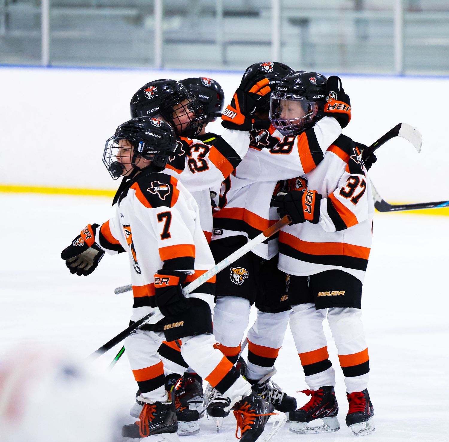 Youth hockey players in black and orange uniforms celebrate together on ice after scoring a goal.