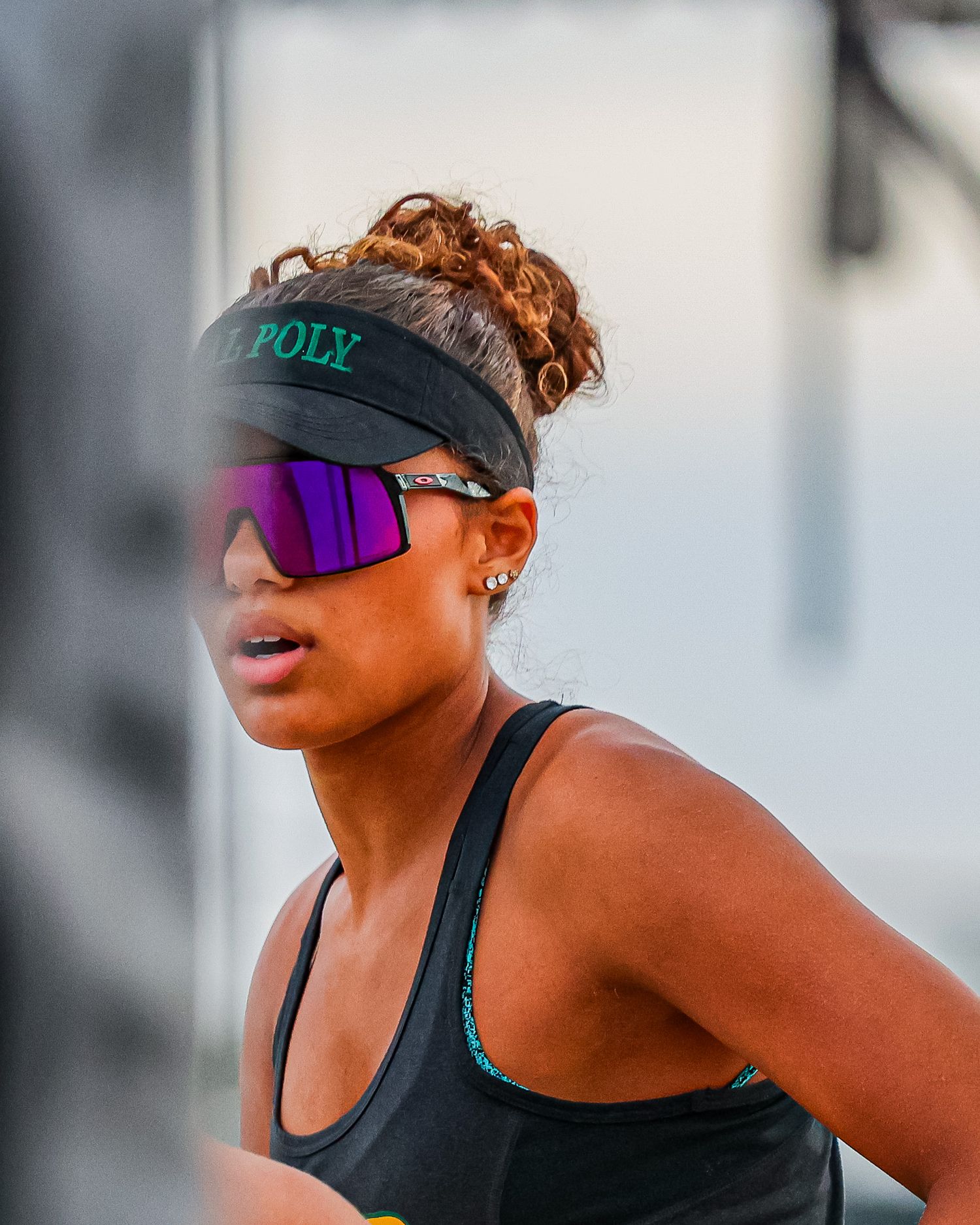 Close-up of female beach volleyball player wearing Cal Poly visor and purple mirrored sunglasses during competition.