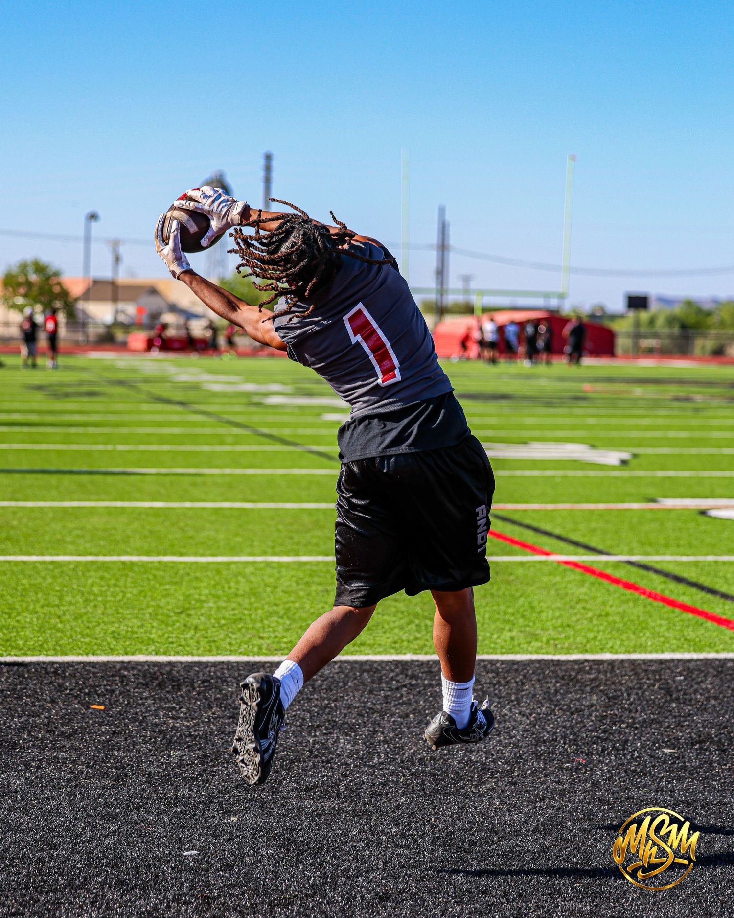 Youth football player #1 jumps to catch football on green turf field during practice.