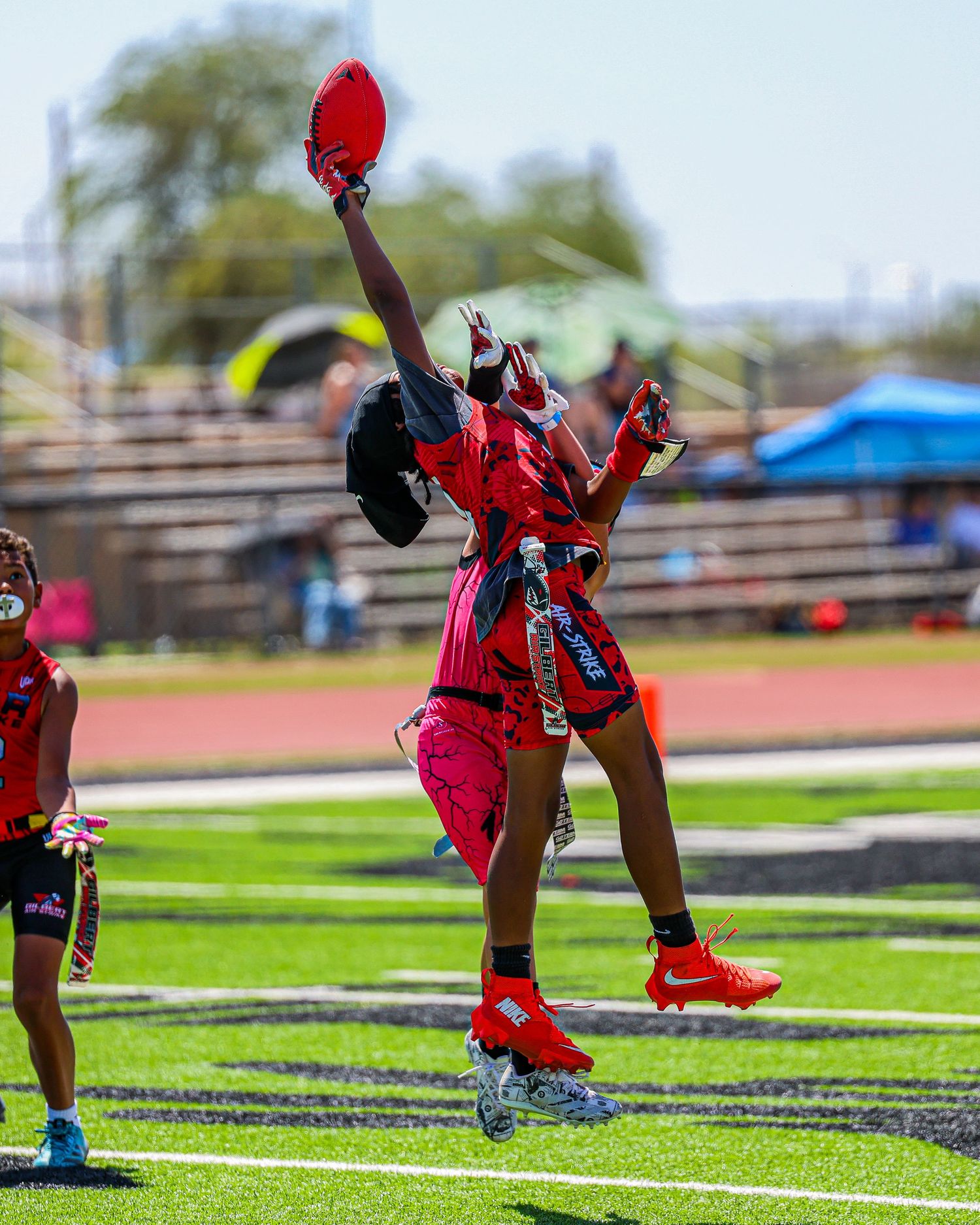 A flag football player in red uniform jumps triumphantly while holding flags during a game.
