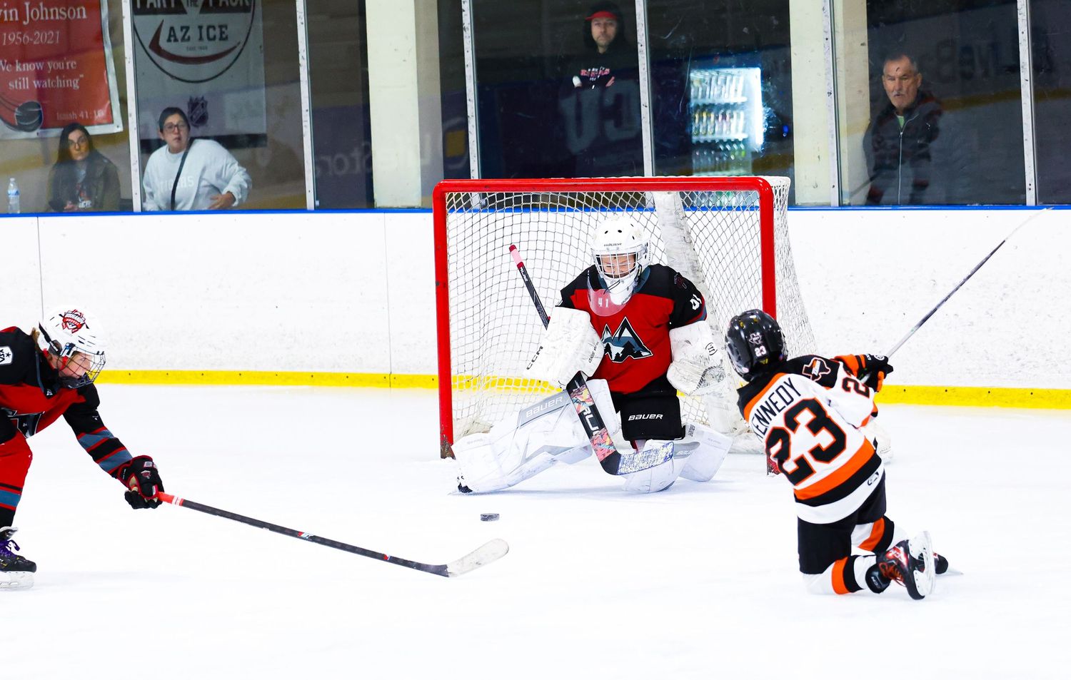 Hockey player number 23 slides on ice near goal as goalie defends during indoor ice hockey game.