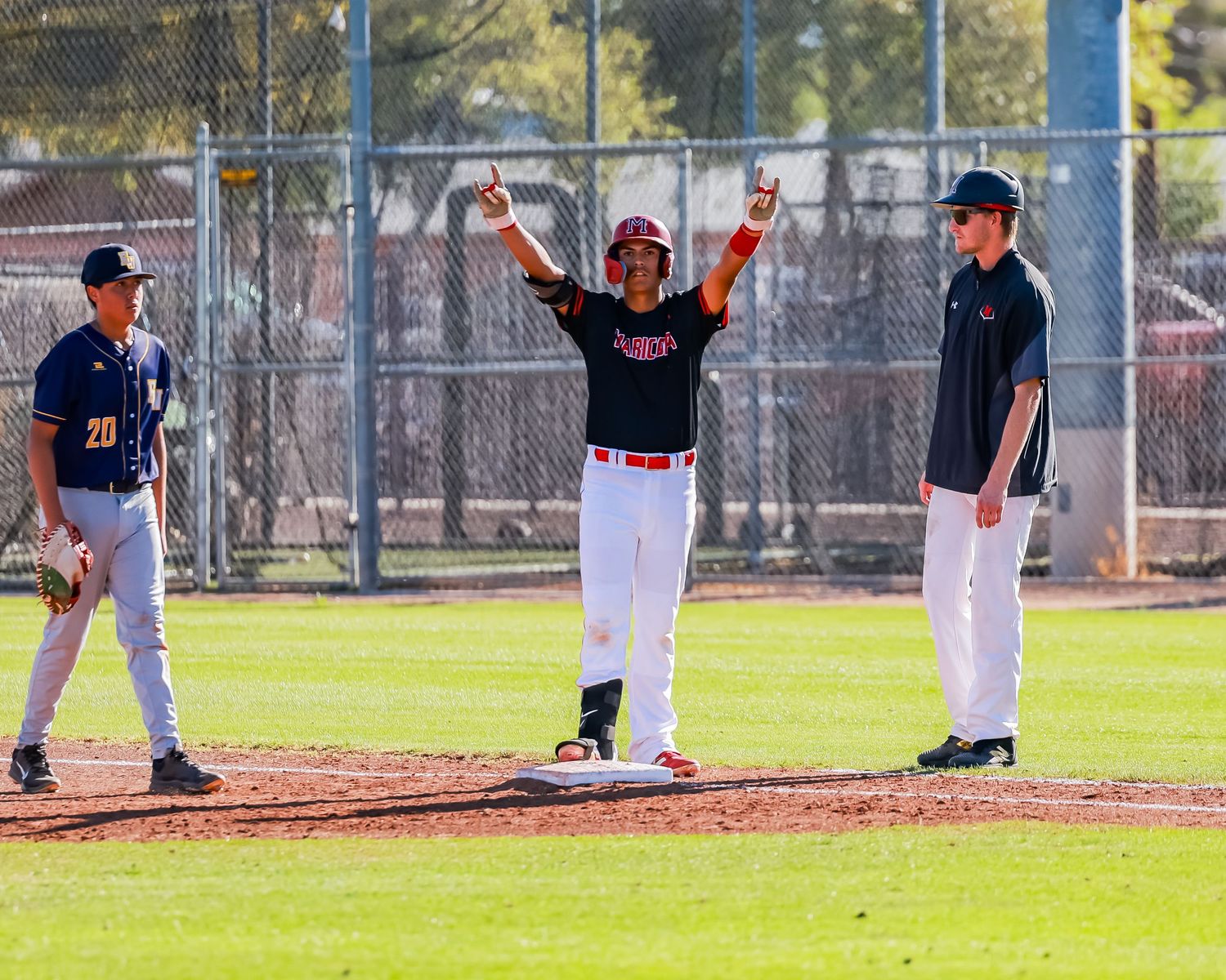 Baseball player in red uniform celebrates hit with arms raised at first base.