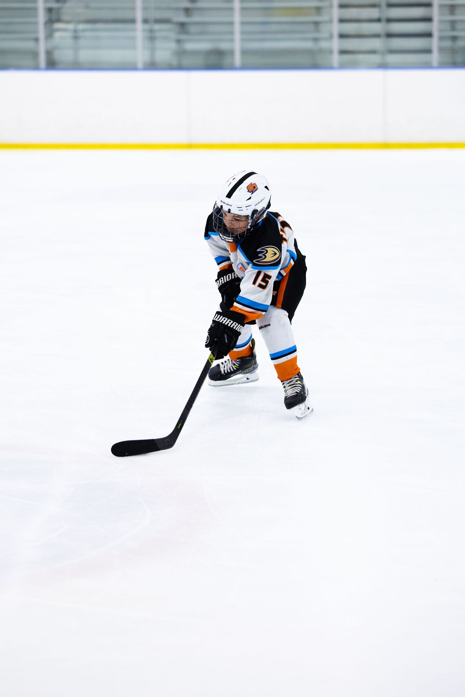 Hockey player number 15 in white and orange Anaheim Ducks uniform skating with puck on indoor ice rink.