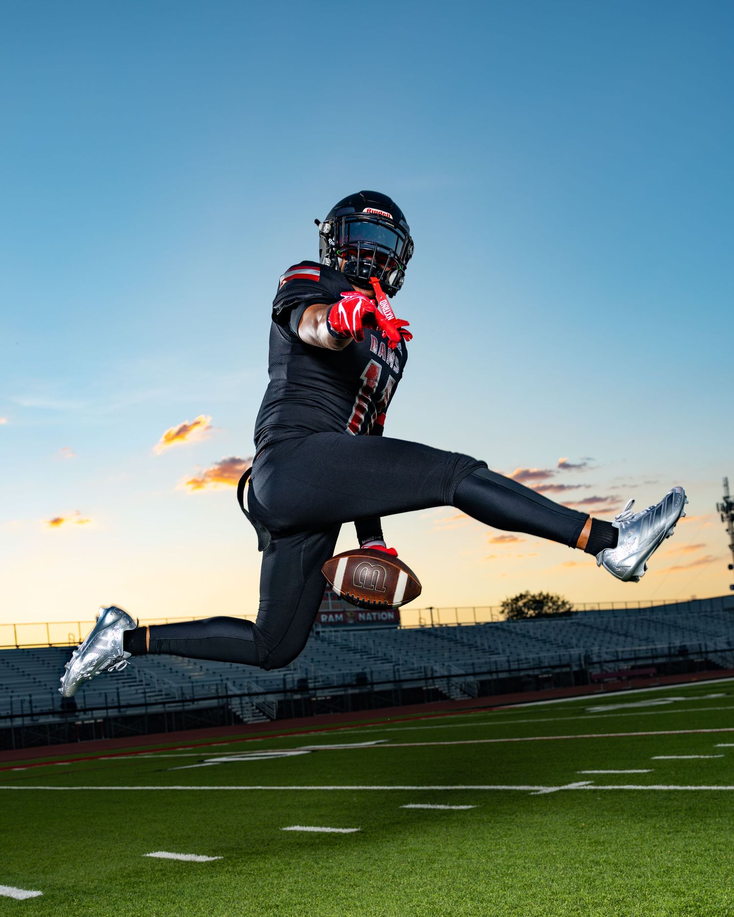 Football player leaps mid-air catching ball at sunset on stadium field.