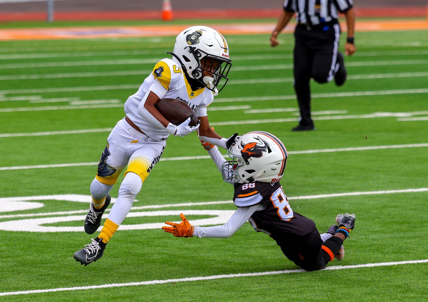 Youth football player in gold jersey stiff-arms defender during tackle attempt in game.