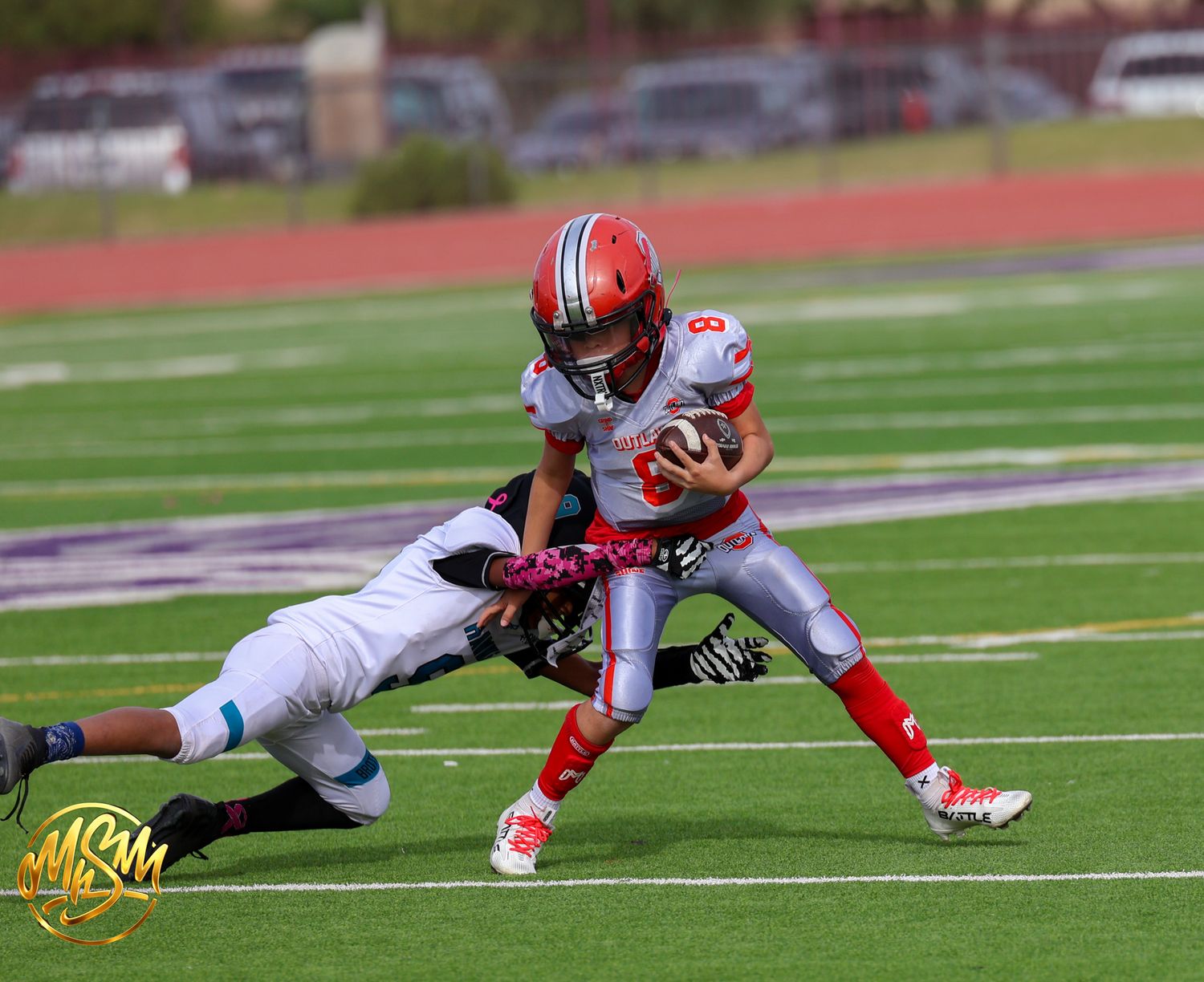 Young football player in red jersey #8 breaks tackle during youth league game.