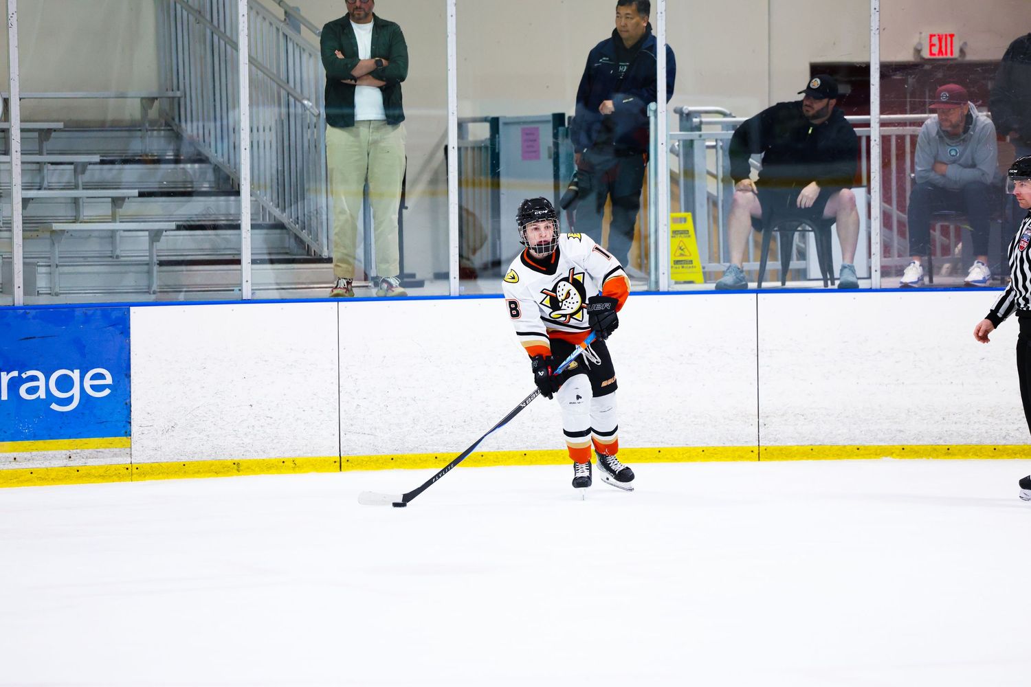 Ice hockey player in orange and white uniform handles the puck during an indoor arena game.