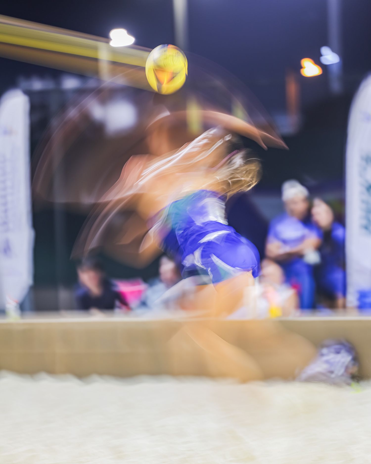 Motion blur action shot of female beach volleyball player diving for the ball during a night match.