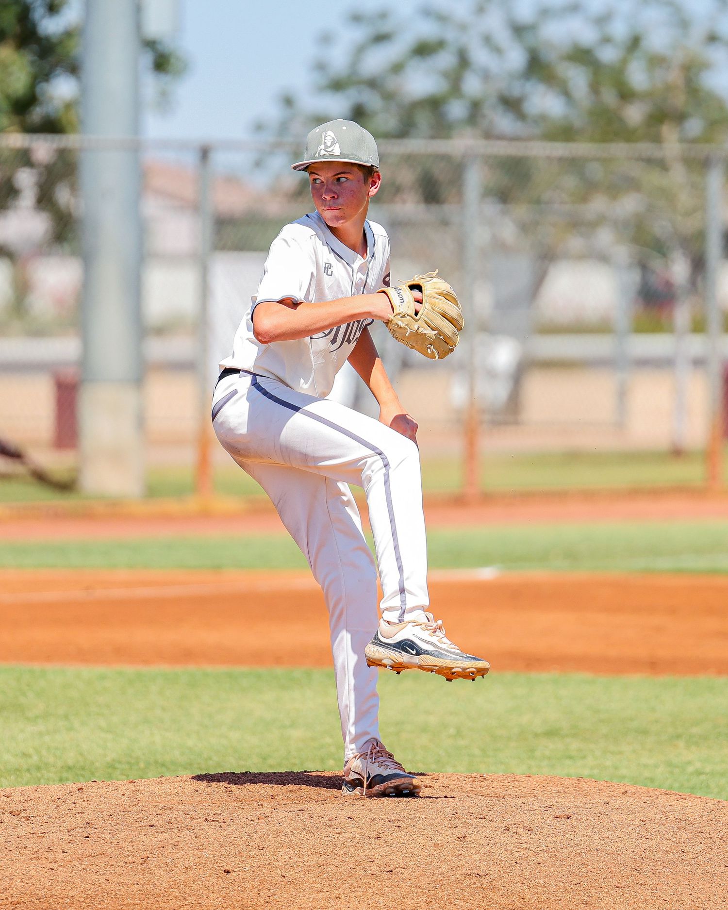 Young baseball pitcher in white uniform preparing to deliver pitch on mound.