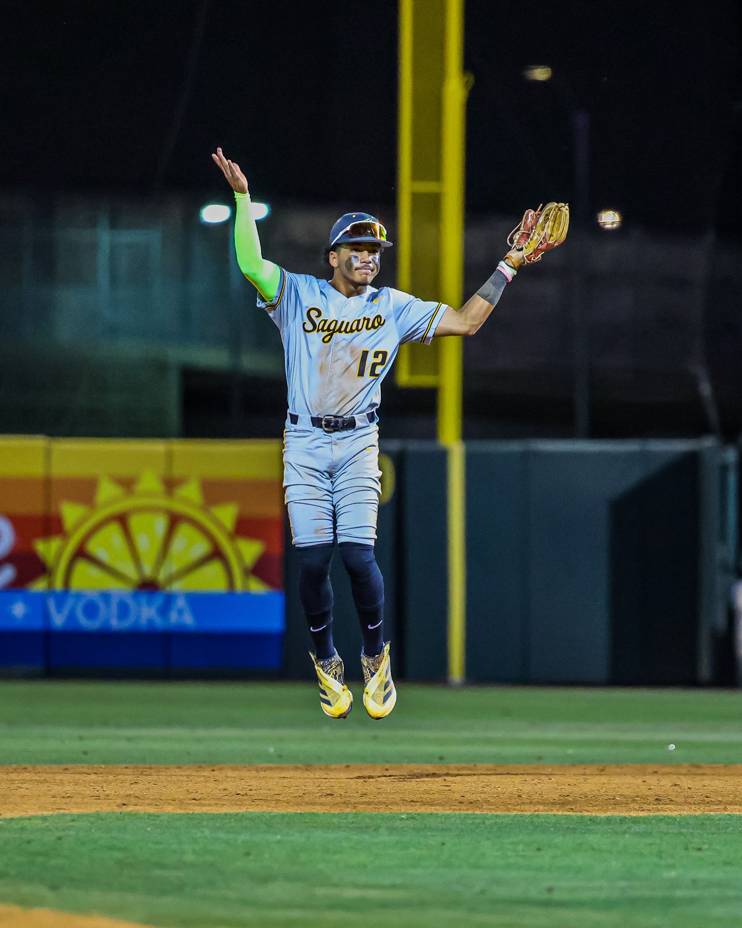 Saguaro player number 12 leaps with arms raised catching ball during night game.