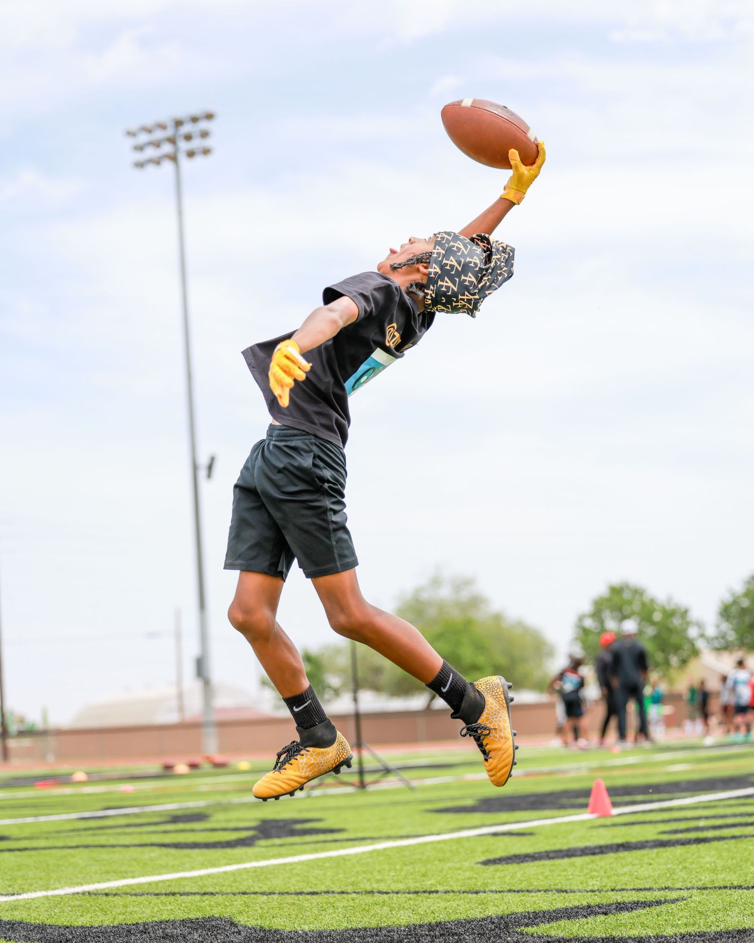 Football player leaps to make a one-handed catch during an outdoor practice on a green turf field.