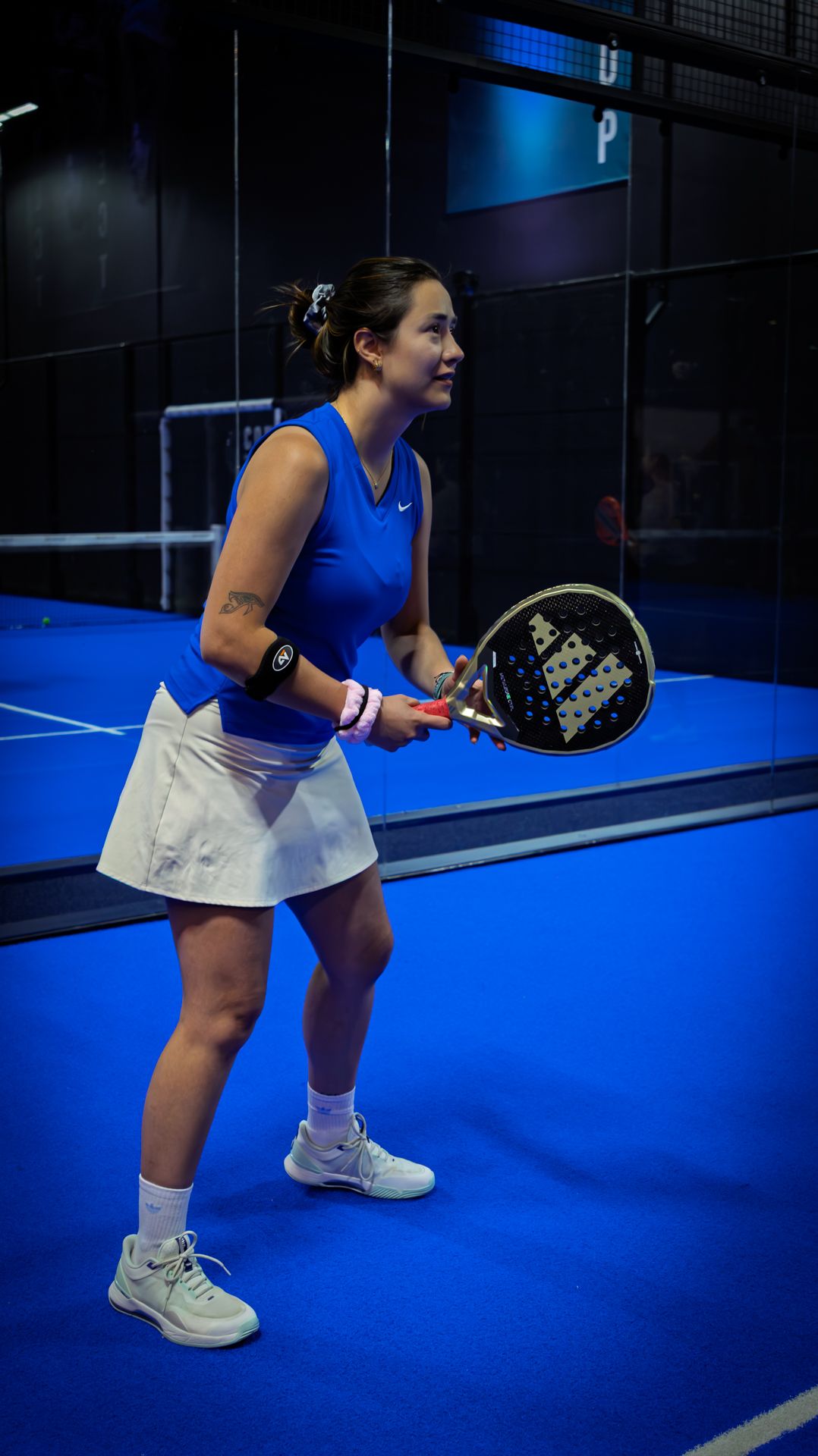 Asian woman in blue Nike tennis outfit holding a padel racket on a blue indoor court.
