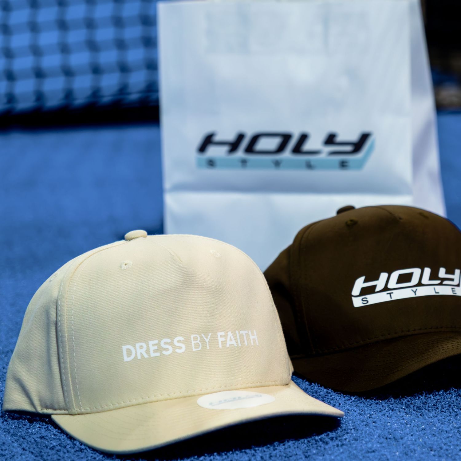Two Holy Style caps, one beige with Dress By Faith text and one dark brown, on a blue surface.
