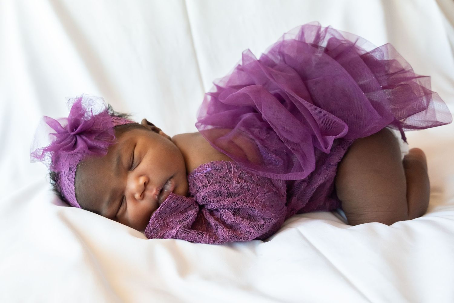 Baby girl with purple dress professionally posed on white blanket