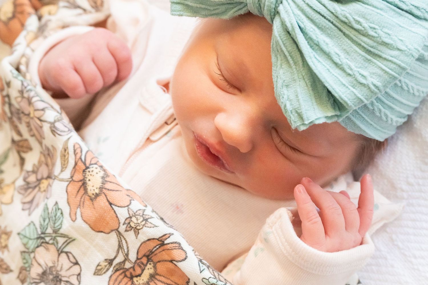 close of portrait of baby girl with eyelashes and bow wrapped in flower blanket by professional photographer in henderson texas