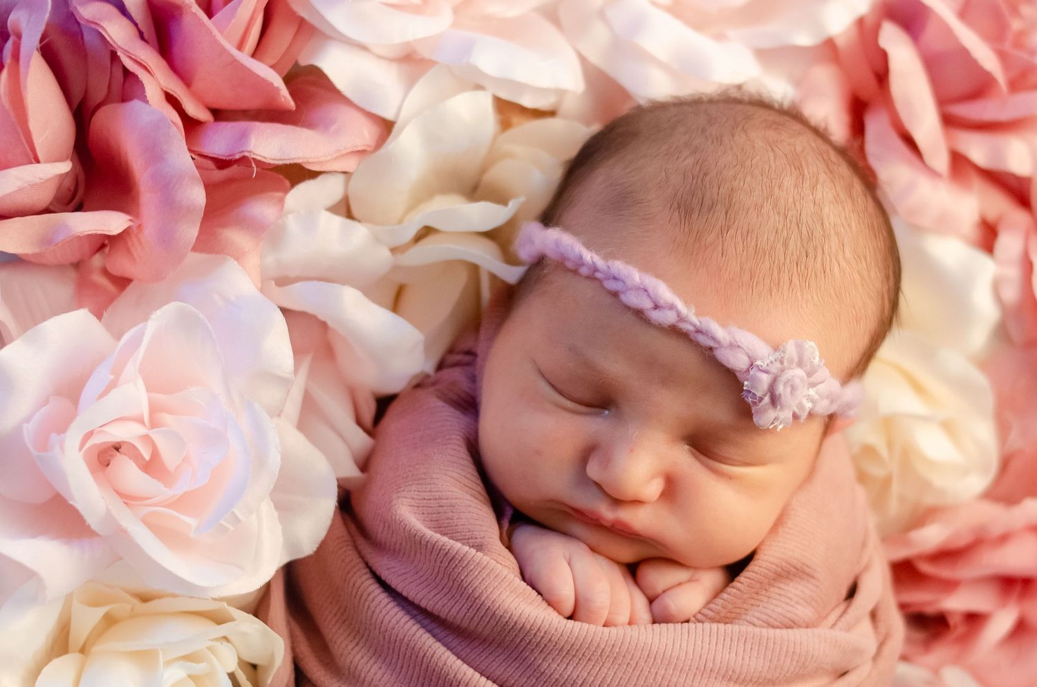 baby girl wrapped in pink with flower head bow on bed of flowers in henderson texas professional photography studio