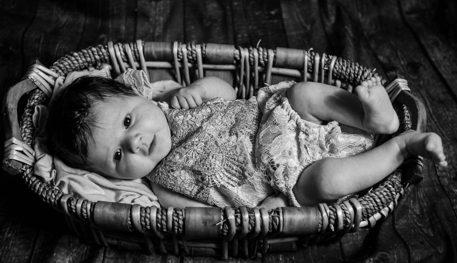 black and white image of newborn girl in wooden basket wearing a lace outfit