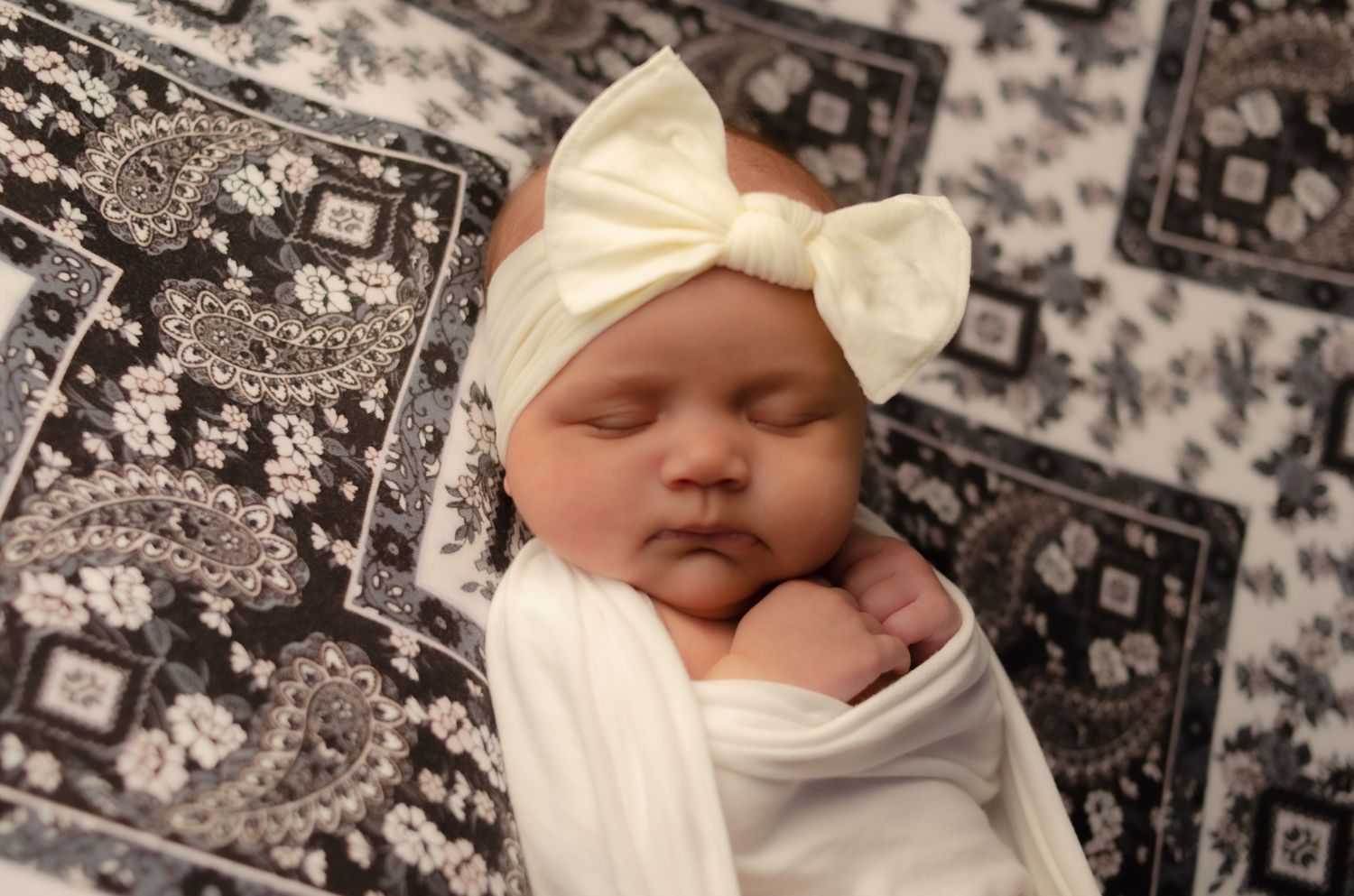 Baby girl swaddled in white with white bow on black and white blanket in Henderson Texas home studio