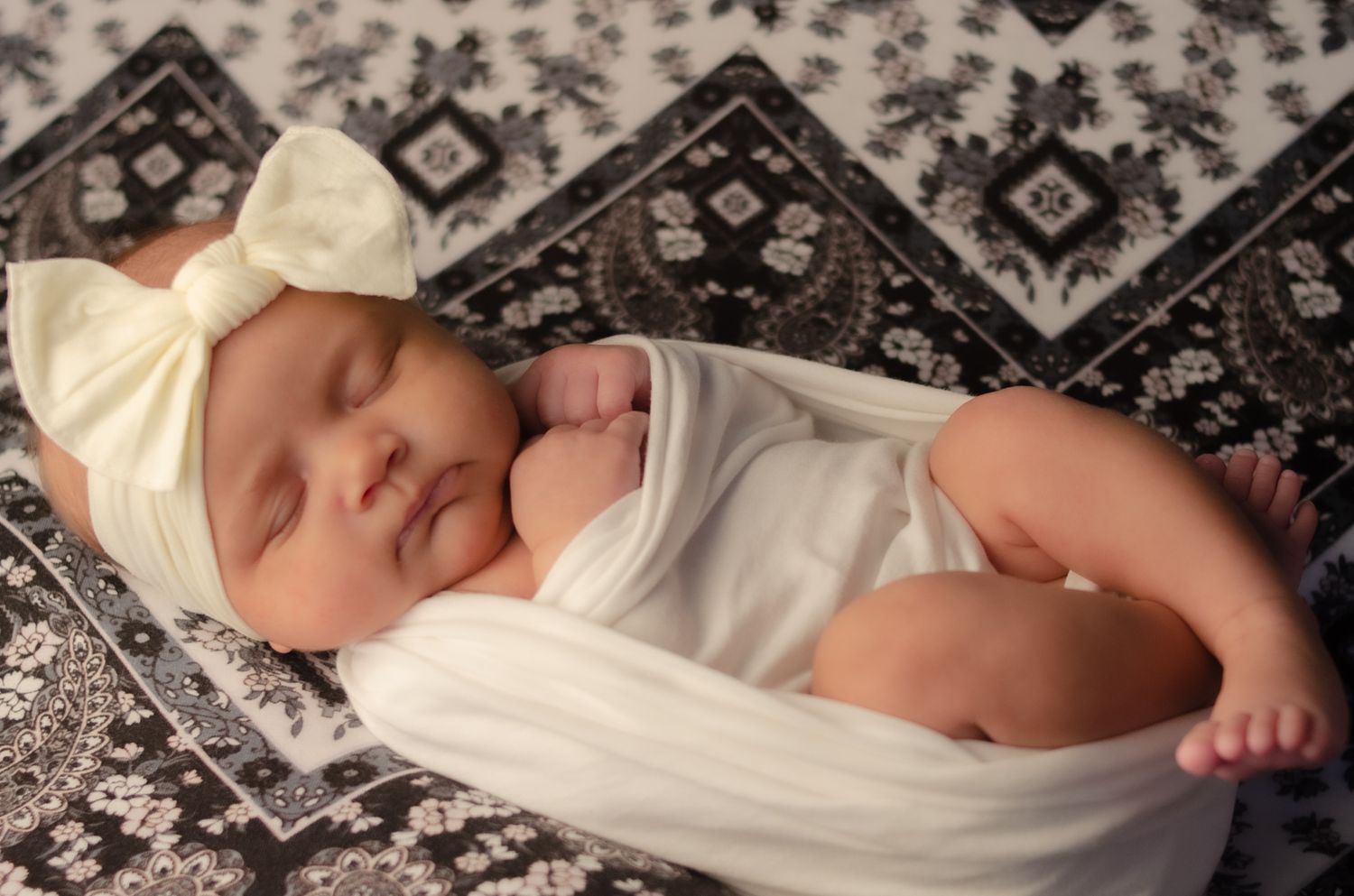 baby girl wrapped in white with white head bow on black and white mandala blanket in newborn portrait