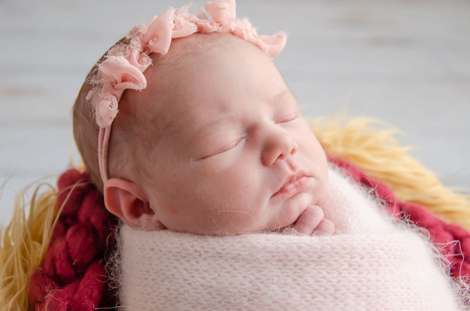 pink head bow on baby girl wrapped in pink cashmere blanket with yellow and red fur underneath
