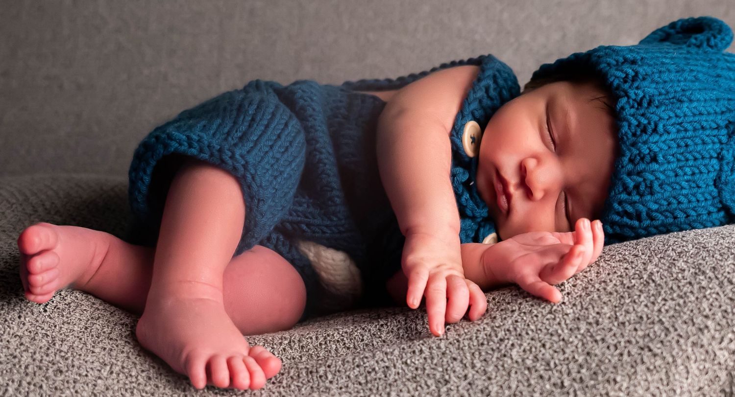 Baby boy dressed in blue overalls with matching hat in newborn photography studio with professional props in henderson