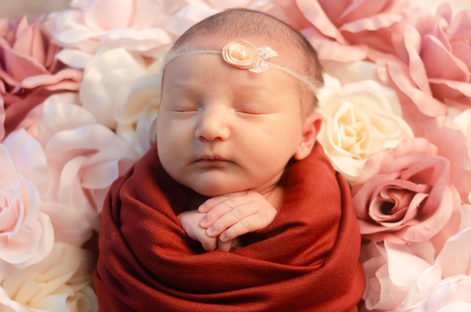 baby girl wrapped in red with flower head bow on bed of flowers in henderson texas professional photography studio