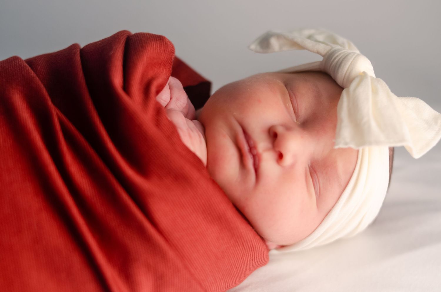 baby girl wrapped in red blanket with white bow in professional photography studio in henderson texas