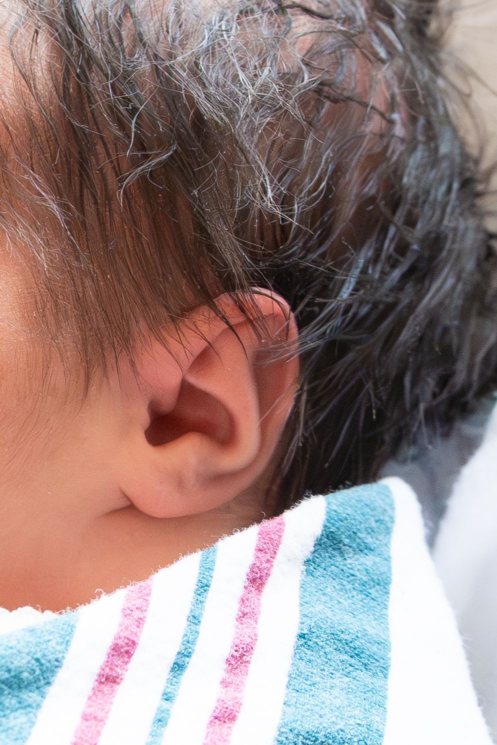 Close up micro detail shot of newborn ear with lots of black hair