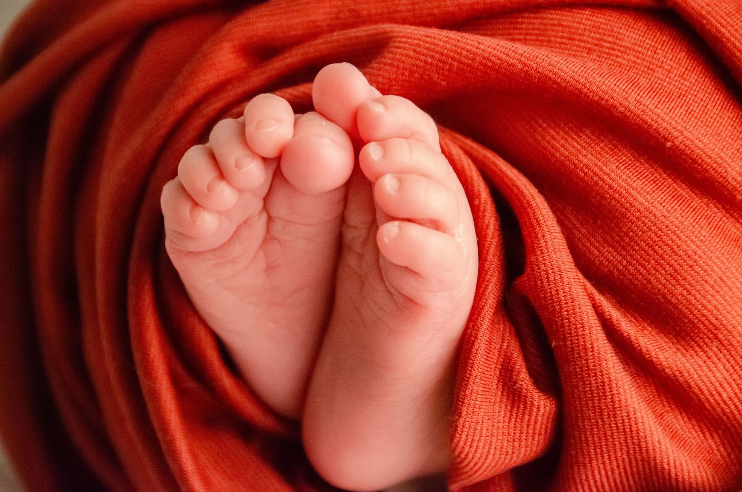 close up micro detail of newborn toes wrapped in red silk blanket from professional newborn prop closet