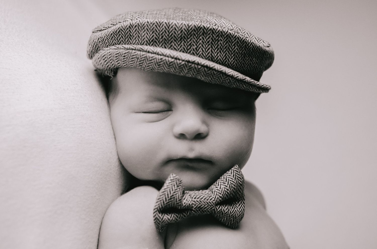 black and white image of baby boy dressed up with top hat and matching bow tie in newborn photography session