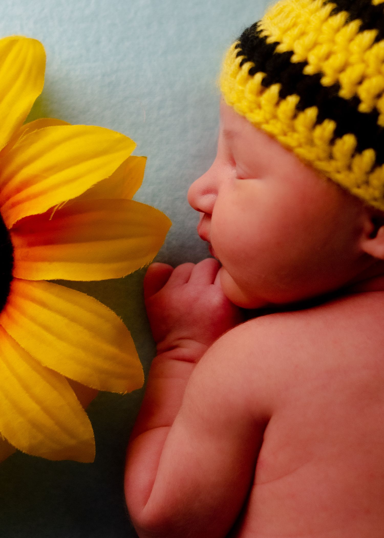 Close-up portrait of a newborn baby's tiny fingers and peaceful expression with  sunflower and matching hat in home studio with photographer