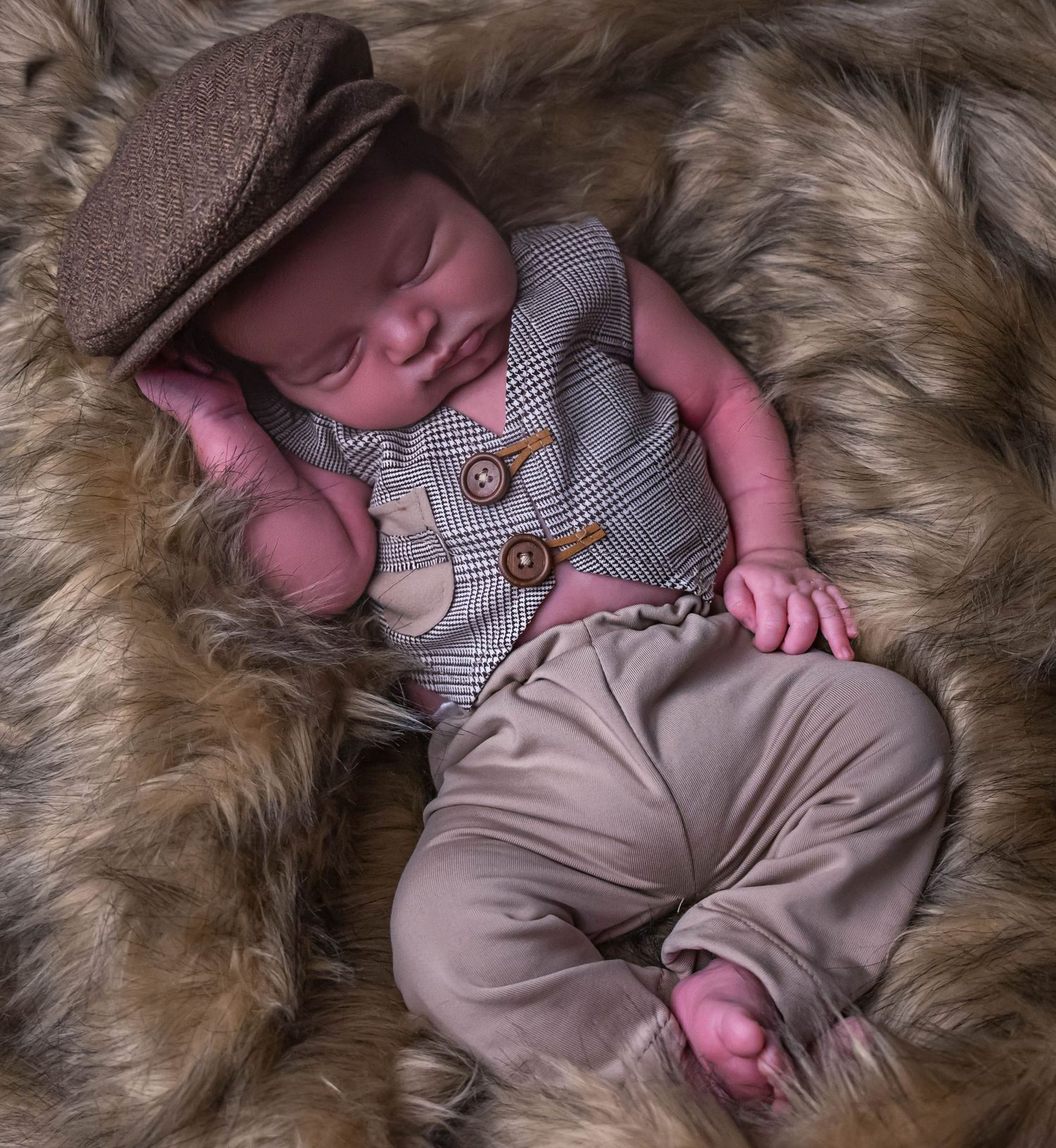baby boy dressed as man with button up vest and matching pants and hat laying on a fur blanket in home photography studio