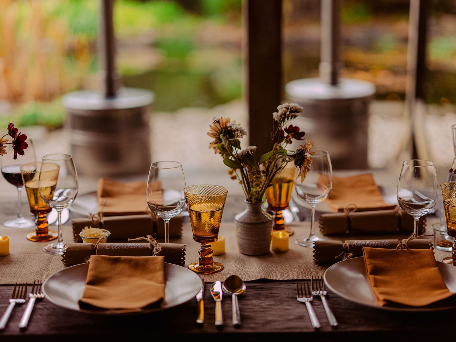 Elegant wedding reception table set with amber glassware, floral centerpiece, and warm candlelight.