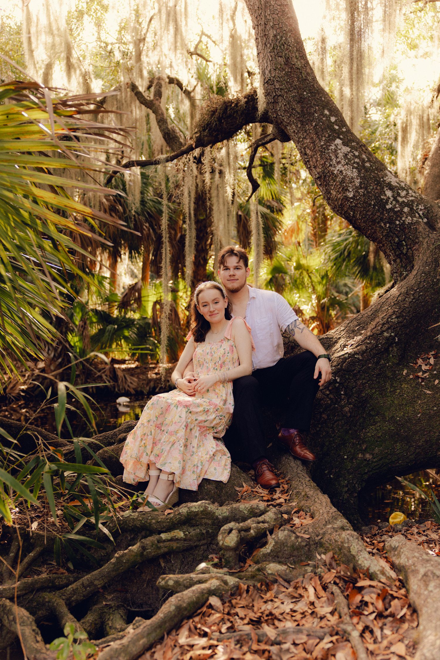 Couple poses romantically against a large mossy tree in a lush Florida botanical garden setting.