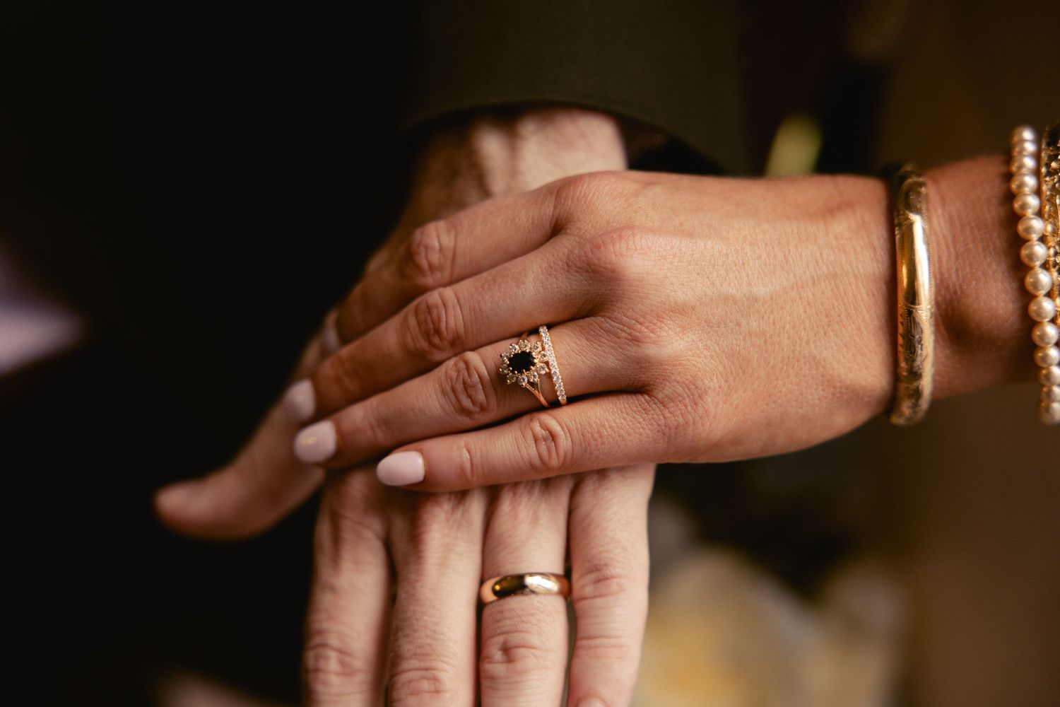 Close-up of couple's hands showing gold wedding band and black stone engagement ring.