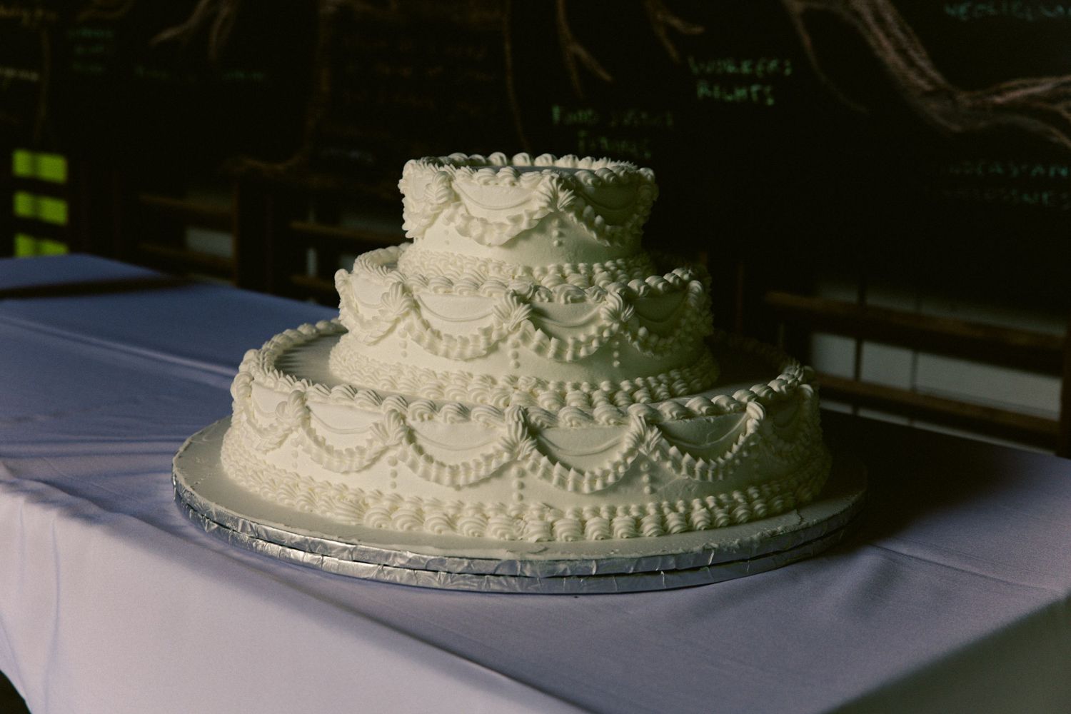 Classic three-tier white wedding cake with scalloped piped frosting displayed on a white tablecloth.