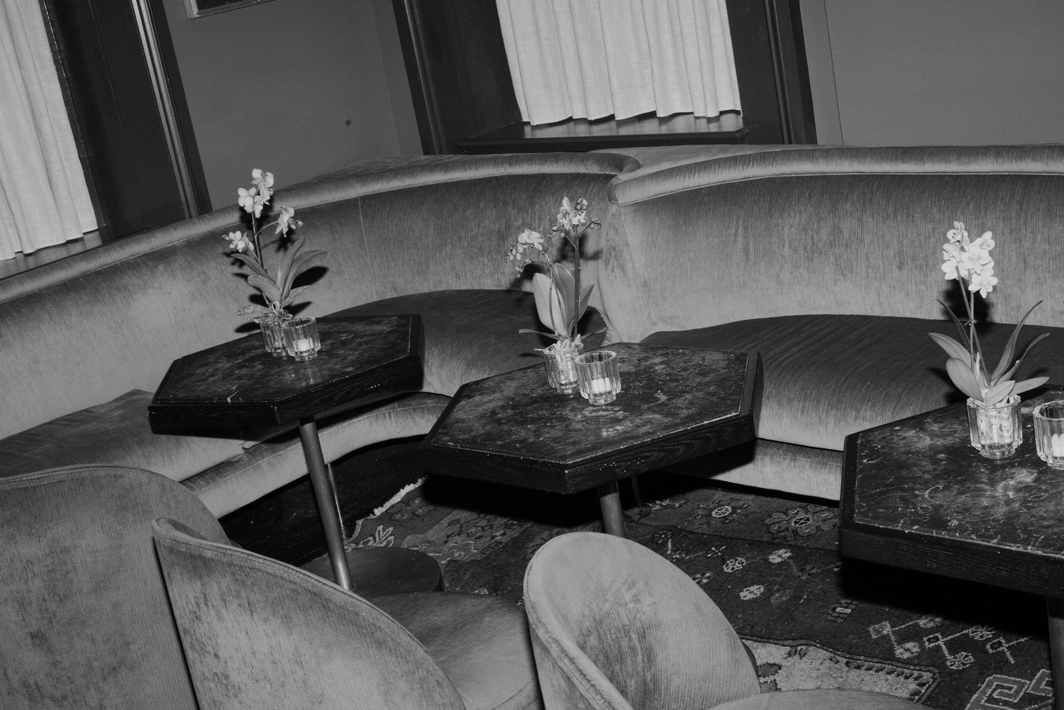 Black and white photo of curved velvet booth seating with marble tables and orchid flowers.