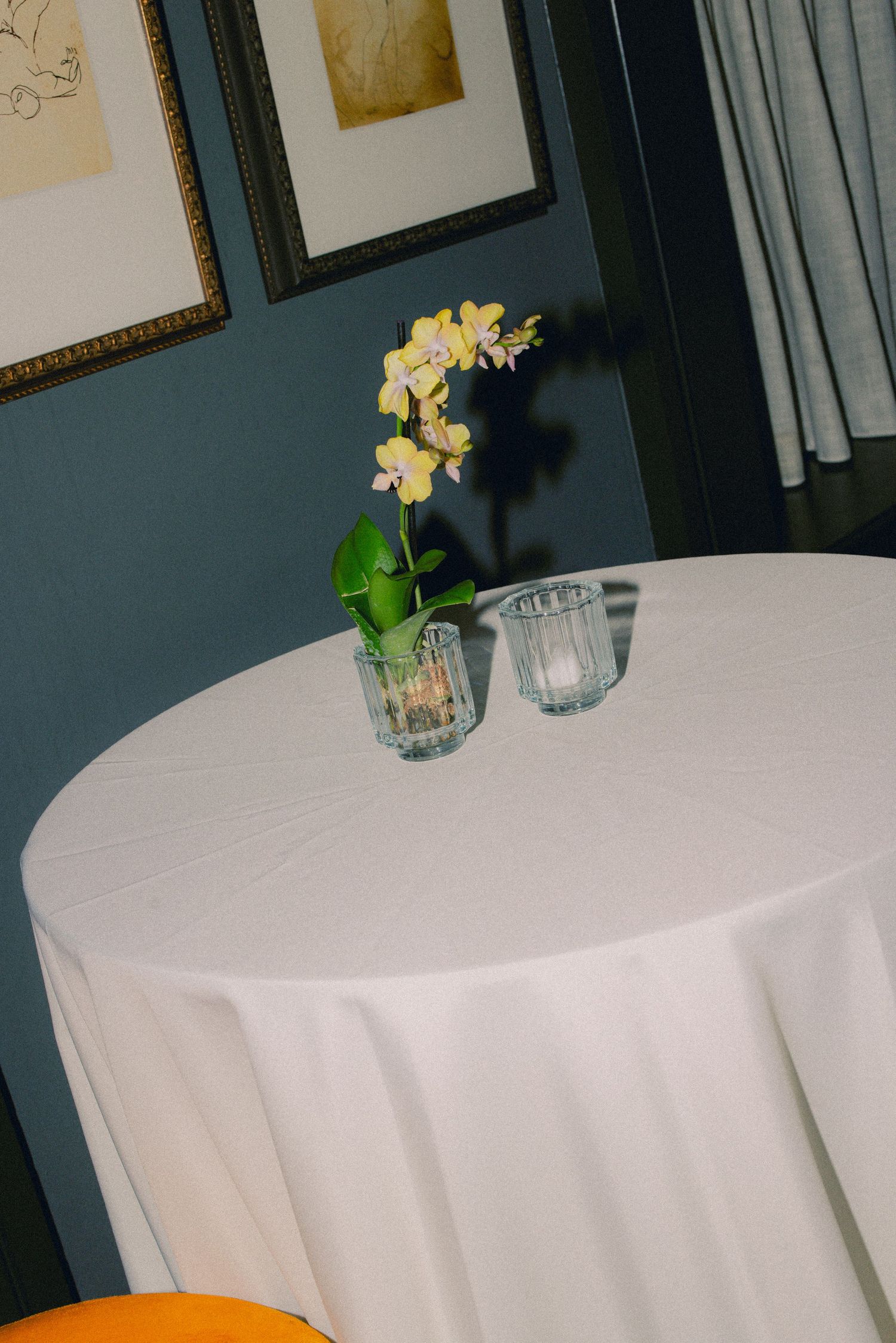 Round white tablecloth-covered cocktail table with yellow orchid centerpiece and glass votives.