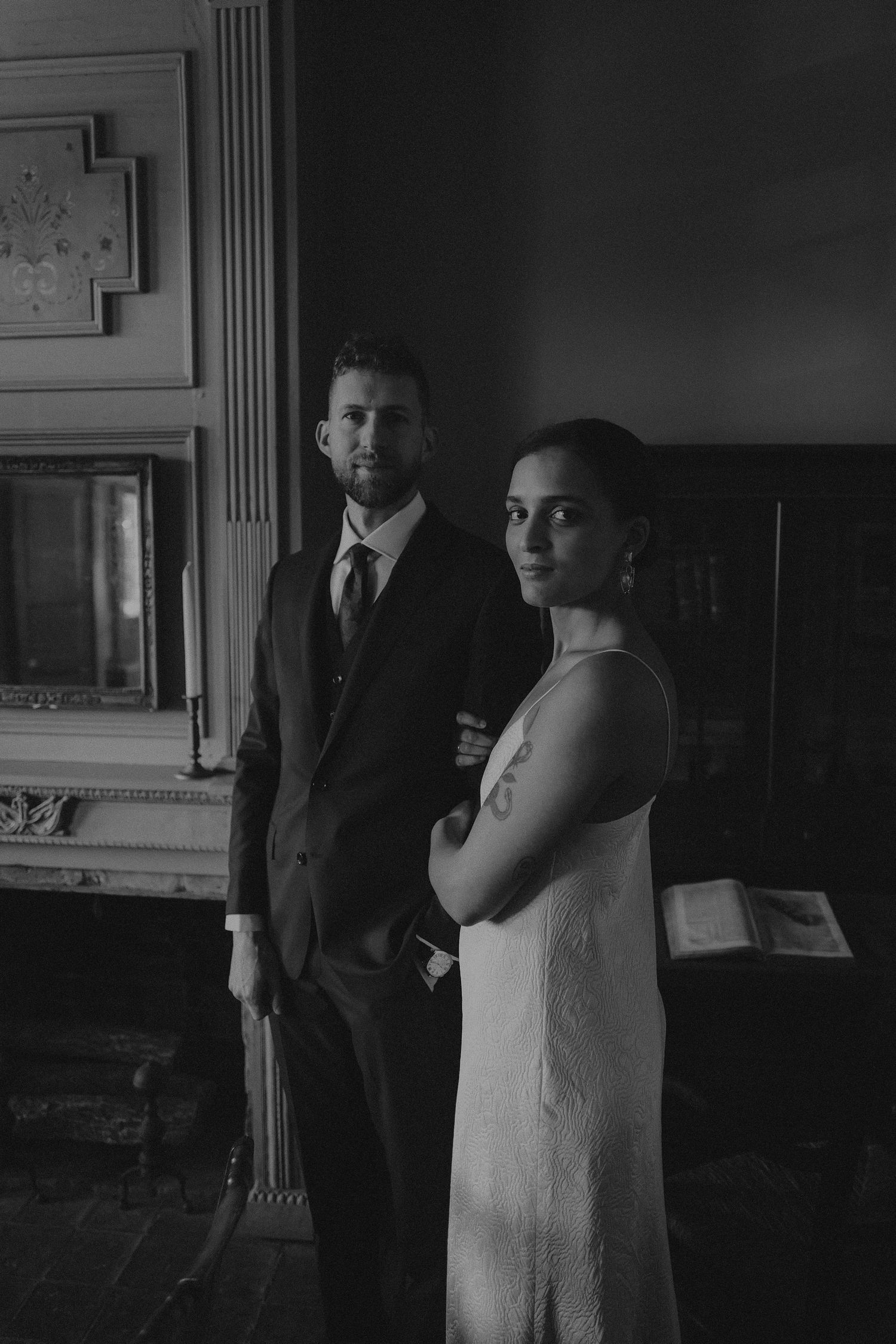 Elegant black and white portrait of bride and groom posing by a fireplace mantel.