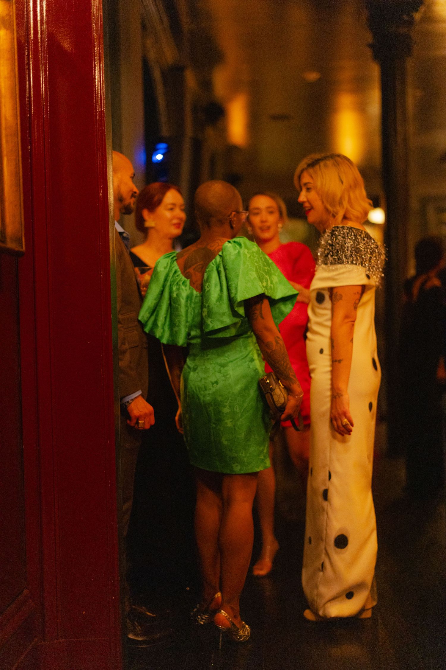Elegantly dressed women in colorful gowns socializing at an upscale evening party event.