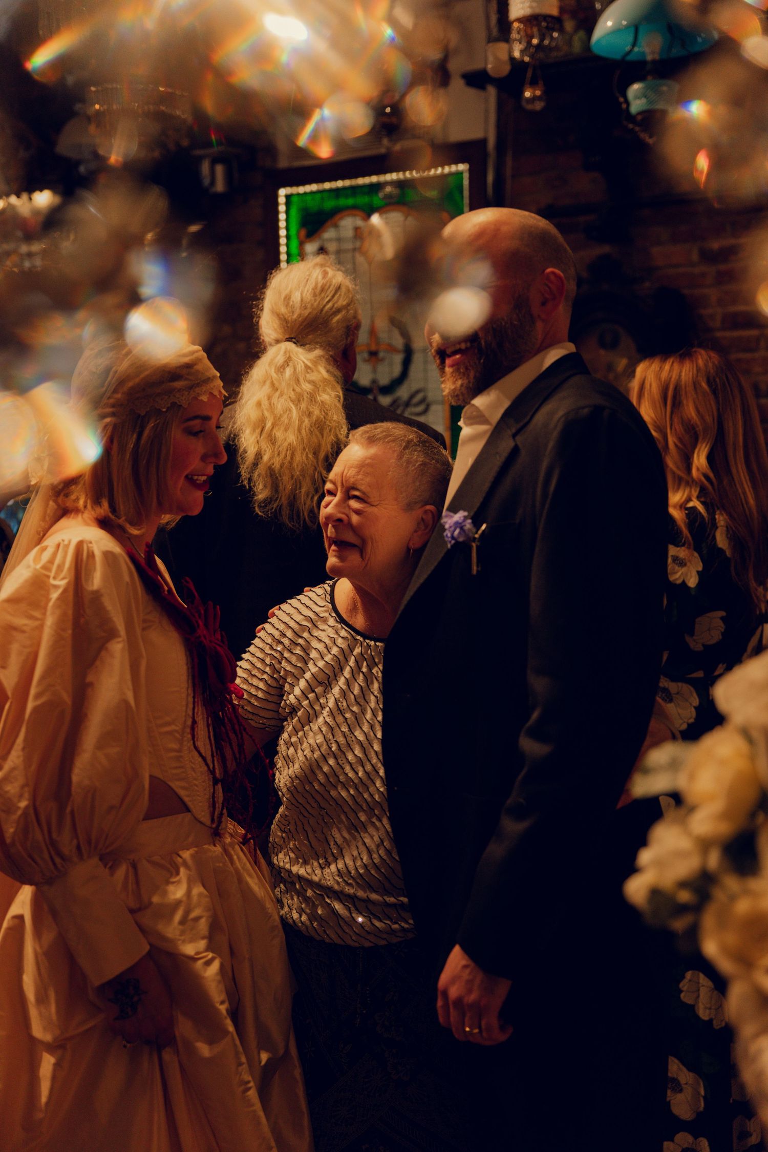 Bride and groom sharing a joyful moment with a guest amid falling confetti at their reception.